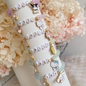 Pode incluir: Cinco pulseiras de contas coloridas com pingentes. Cada pulseira tem um nome diferente escrito em letras douradas: Lily, Rose, Indie, Daisy e Sage. Os pingentes incluem uma estrela, um cora&ccedil;&atilde;o e um personagem de desenho animado.