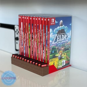 May include: A brown brick-shaped stand with a red base holds a collection of Nintendo Switch game cartridges and cases. The cases are mostly red and feature various game titles, including "The Legend of Zelda: Link's Awakening".
