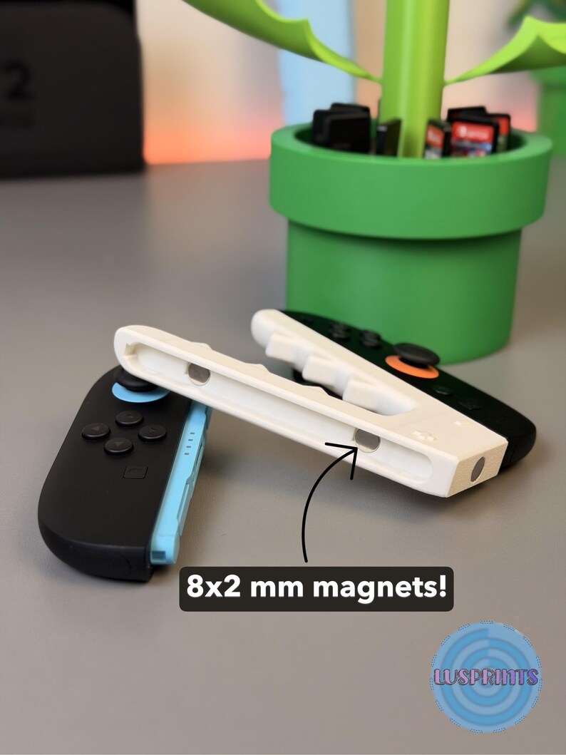 May include: A black and blue Nintendo Switch Joy-Con controller next to a white controller grip. The image also shows a green Mario-themed planter with game cartridges. The text in the image says "8x2 mm magnets!"