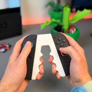 May include: Black and white gaming controller with a unique design, held in hands. The controller features buttons and a joystick. The design includes a white center section with a jagged edge. The controller is for a gaming console.