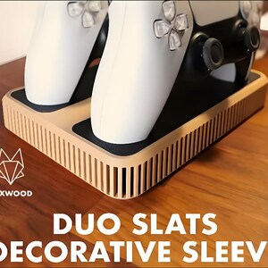 May include: A wooden decorative sleeve for two game controllers. The sleeve has a light brown, slatted design and holds two white controllers. The text "DUO SLATS DECORATIVE SLEEVE" is displayed on the bottom.