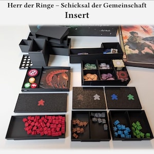 Könnte beinhalten: Schwarzer Spieleinsatz mit verschiedenen Fächern und Tabletts. Enthält Behälter für Spielsteine in verschiedenen Farben, darunter Rot, Braun, Blau und Grün. Der Einsatz dient zur Organisation der Spielkomponenten.