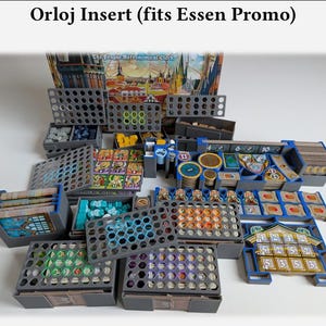 Może przedstawiać: Szary i niebieski organizer do gry planszowej, oznaczony jako "Orloj Insert (fits Essen Promo)". Wkładka posiada wiele przegródek i tacek na elementy gry, w tym karty, żetony i miniatury. Pudełko z grą jest widoczne w tle.