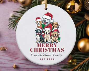 May include: A white ceramic Christmas ornament featuring a group of dogs wearing Santa hats. The ornament has the text "MERRY CHRISTMAS" and "From The Miller Family - EST 2024" in burgundy. A gold string is attached for hanging.