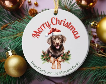 May include: A white ceramic Christmas ornament with a watercolor image of a brown dog wearing a Santa hat. The words "Merry Christmas" are in red script above the dog. The text "From Charly and the Mercado family" is below the dog.