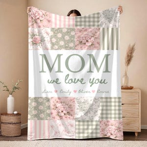 May include: A patchwork blanket with floral and striped patterns in pink, white, and green. The blanket features the text "MOM we love you" with names below. A decorative and personalized gift.