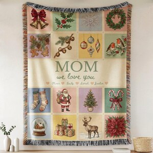 May include: A woven throw blanket featuring a grid of Christmas-themed illustrations including bells, holly, ornaments, robins, stockings, Santa Claus, a tree, candy canes, a snow globe, gifts, a reindeer, and a poinsettia. Text reads MOM we love you.