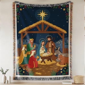 May include: A woven throw blanket featuring a colourful nativity scene with the Holy Family, three wise men, a donkey, and a cow under a bright star. The design includes a dark blue night sky, a wooden stable, and decorative fringe on the edges.