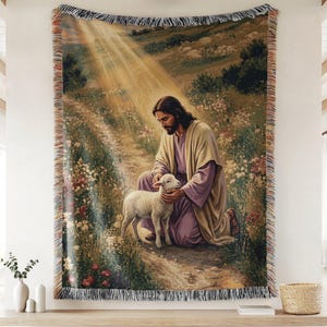May include: A woven tapestry throw blanket featuring a depiction of a bearded figure in a tan robe and purple tunic kneeling in a field of flowers, gently holding a small white lamb. A bright beam of light shines down from above on the scene.