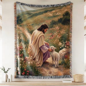 Könnte beinhalten: Eine gewebte Wandteppich-Decke mit der Darstellung einer Figur mit langem braunem Haar und Bart, die ein beiges Gewand über einem violetten Kleidungsstück trägt und auf einem Feldweg inmitten bunter Wildblumen kniet und ein weißes Lamm berührt.