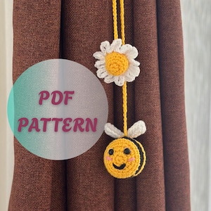 May include: A yellow crocheted curtain tieback featuring a daisy and a smiling bee. The daisy has white petals and a yellow center. The bee is yellow and black with white wings. The text "PDF PATTERN" is in a teal circle.