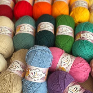 May include: A collection of colorful yarn skeins in various shades, including red, orange, yellow, green, blue, pink, and purple. Each skein is labeled with "alize Cotton Gold". Ideal for knitting and crochet projects.