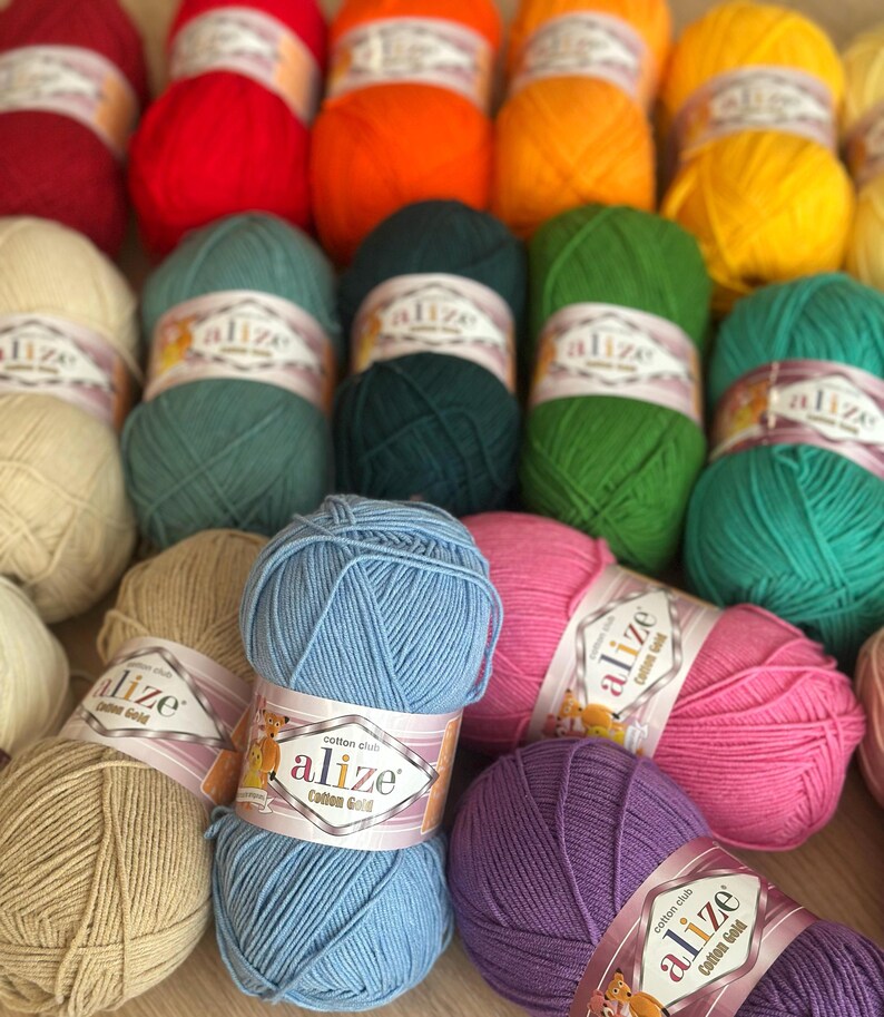 May include: A collection of colorful yarn skeins in various shades, including red, orange, yellow, green, blue, pink, and purple. Each skein is labeled with "alize Cotton Gold". Ideal for knitting and crochet projects.