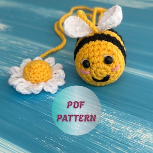 May include: A crocheted bee with black and yellow stripes, white wings, and a smiling face. A crocheted daisy is next to the bee. The image includes the text "PDF PATTERN" in a circle.