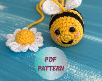 May include: A crocheted bee with black and yellow stripes, white wings, and a smiling face. A crocheted daisy is next to the bee. The image includes the text "PDF PATTERN" in a circle.