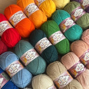 以下が含まれることがあります： 赤、オレンジ、黄色、緑、青、ベージュなど、さまざまな色合いのAlize Cotton Goldのカラフルな毛糸玉のコレクション。各毛糸玉にはブランドラベルが巻かれています。編み物や手編みプロジェクトに最適です。