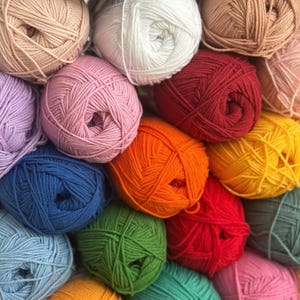 May include: A collection of colorful yarn balls in various shades, including pink, white, red, orange, green, and blue. The yarn is tightly wound, creating a textured surface. Ideal for knitting and crochet projects.