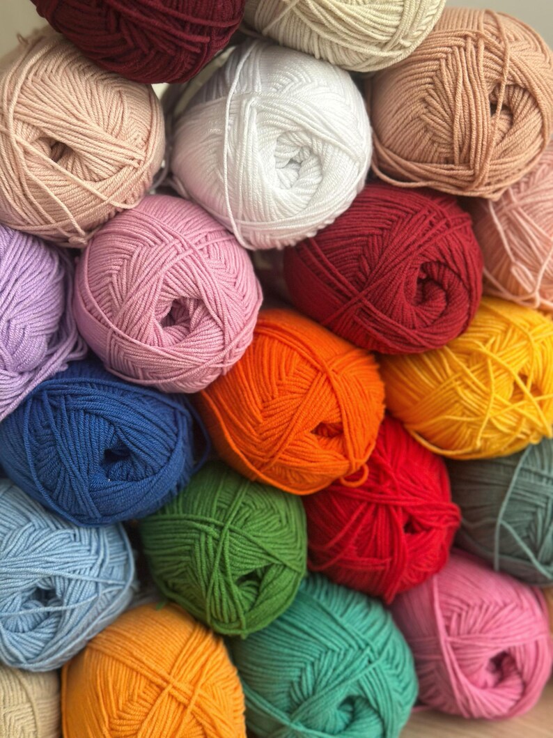 May include: A collection of colorful yarn balls in various shades, including pink, white, red, orange, green, and blue. The yarn is tightly wound, creating a textured surface. Ideal for knitting and crochet projects.