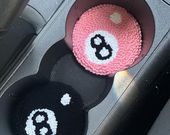 Può includere: Due sottobicchieri fatti a mano per auto, uno rosa e uno nero, ciascuno con un disegno all'uncinetto di una palla otto. Il sottobicchiere rosa ha un punto bianco e il numero otto nero. Il sottobicchiere nero ha un punto bianco e il numero otto bianco.