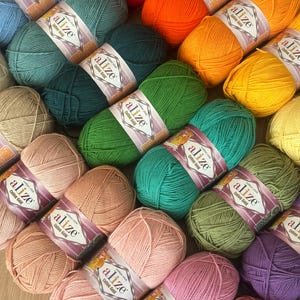 May include: A collection of colorful yarn skeins in various shades, including red, orange, green, and pink. Each skein is labeled with "alize Cotton Gold". The yarn is arranged in a visually appealing display, perfect for knitting and crochet projects.