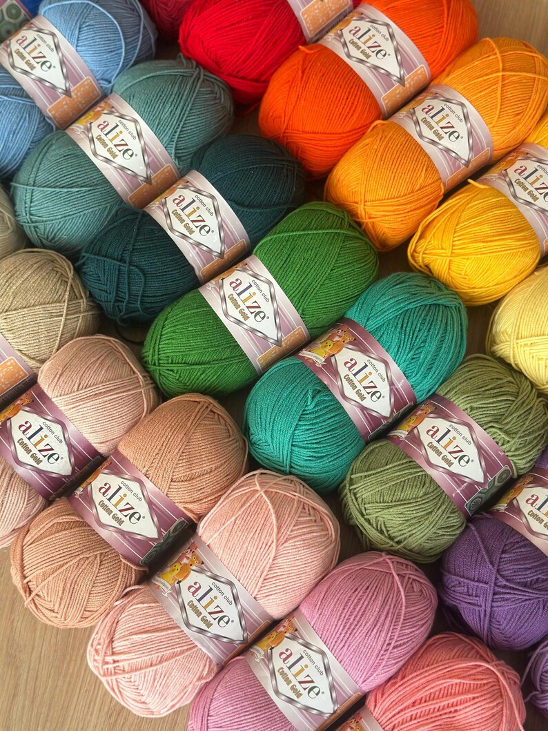 May include: A collection of colorful yarn skeins in various shades, including red, orange, green, and pink. Each skein is labeled with "alize Cotton Gold". The yarn is arranged in a visually appealing display, perfect for knitting and crochet projects.