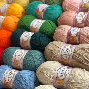 May include: A collection of colorful yarn skeins in various shades, including yellow, green, pink, and blue. Each skein is labeled with the brand name "alize Cotton Gold". The yarn is neatly arranged, suggesting a craft supply or textile product.