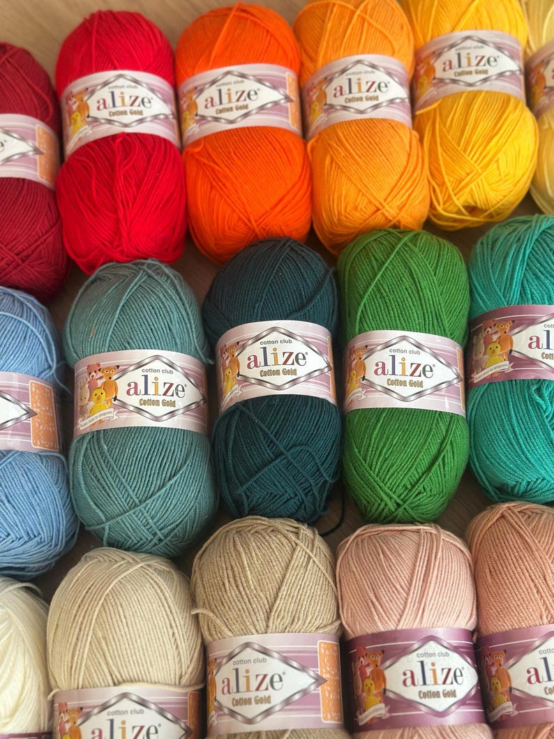 May include: A collection of colorful Alize Cotton Gold yarn skeins. The yarn is available in various shades, including red, orange, yellow, green, and blue. Each skein is labeled with the brand name and product details. Ideal for knitting and crochet projects.