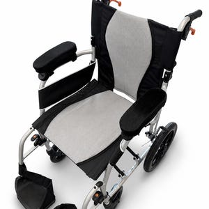 May include: A wheelchair with a silver metal frame, black armrests, and a grey mesh seat and backrest. It features black fabric side panels, two black footrests, and black wheels. The handles have orange accents, and the design includes a structured back support.