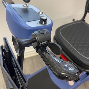 May include: A close-up of a blue mobility scooter featuring a black seat and a carbon fibre-style handle. The scooter has a horn and a control panel with a key and a dial. Designed for mobility and ease of use.
