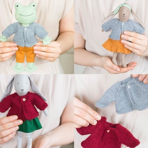 Handmade knitted cardigans worn by soft fabric dolls, shown on a frog doll and bunny dolls, demonstrating fit and style on different characters.