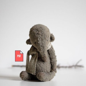 May include: A handmade gray plush elephant toy with a small scarf around its neck. The elephant has large ears and a trunk. A PDF icon is in the lower left corner. The toy is sitting on a white surface.