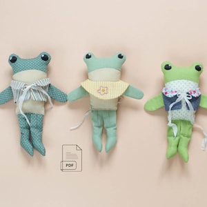 May include: Three stuffed frog dolls made of fabric. The left frog is teal with white polka dots and a striped vest. The center frog is light green with a yellow gingham bib. The right frog is lime green with a floral collar and denim vest.