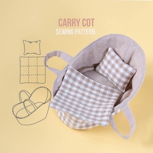 May include: A carry cot sewing pattern featuring a beige fabric carry cot with a brown and white gingham pillow and blanket. The image includes a line drawing illustration of the cot, pillow, and blanket with the text CARRY COT SEWING PATTERN.