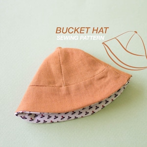 Peut inclure: Un chapeau bob brun avec une doublure à motifs blancs et noirs. Le chapeau est fait d'un tissu doux et texturé. Le texte "BUCKET HAT SEWING PATTERN" est écrit au-dessus du chapeau.