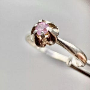 Puede incluir: Un anillo de plata con una piedra preciosa rosa engastada en un diseño con forma de flor.