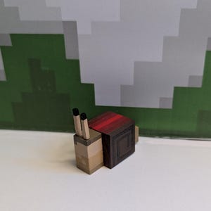 May include: A wooden snail figurine with a pixelated design. The snail's body is light brown, with a dark brown shell and red stripes. It has two black antennae. The background features a pixelated green and white design.