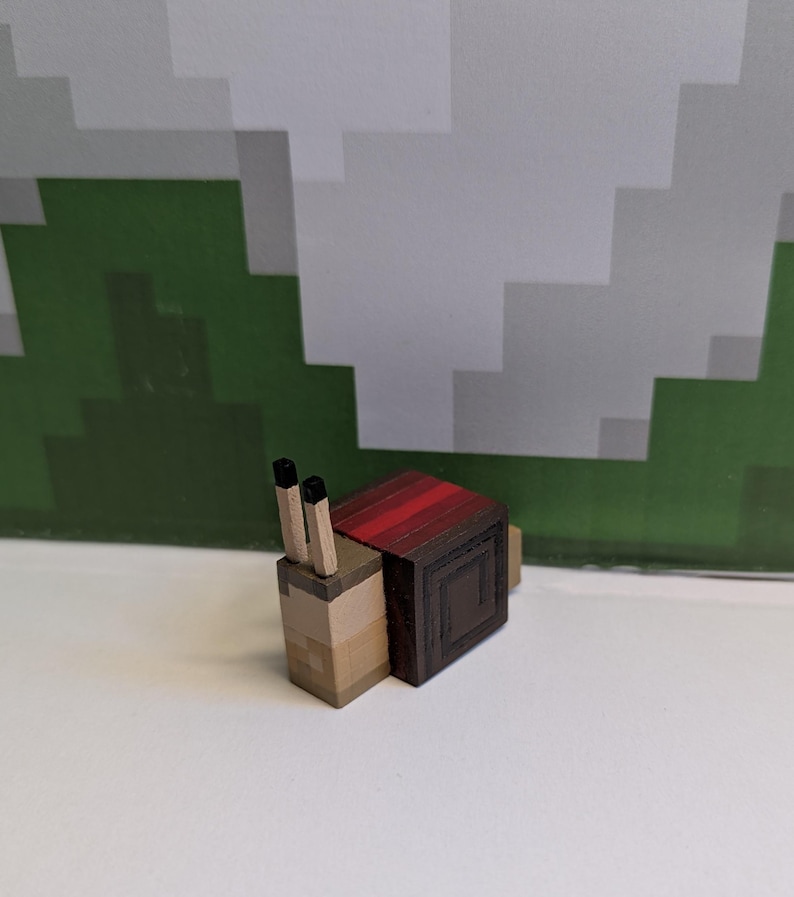 May include: A wooden snail figurine with a pixelated design. The snail's body is light brown, with a dark brown shell and red stripes. It has two black antennae. The background features a pixelated green and white design.