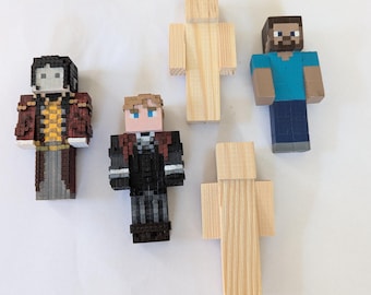 Könnte beinhalten: Vier blockartige, pixelige Figuren auf einer Oberfläche. Zwei Figuren sind mit detaillierten Merkmalen bemalt, darunter eine mit rotem Mantel und eine mit blauem Hemd. Zwei weitere Figuren bestehen aus unbehandeltem, hellem Holz.