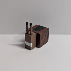 May include: A brown, blocky snail figurine with a square body and a rectangular head. The snail has two black antennae and a white stripe on its head. The body features a series of concentric square patterns.