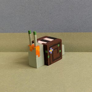 May include: A pixelated snail figurine with a brown shell and a light green body. The shell has a decorative pattern with a pink stripe and a square design. The snail's antennae are green and orange.