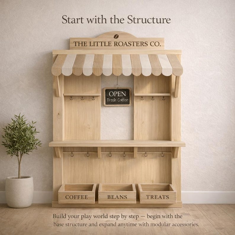 May include: Wooden play structure with a striped awning, hooks, and three labeled bins: "COFFEE," "BEANS," and "TREATS." A small chalkboard sign reads "OPEN Fresh Coffee." The text "THE LITTLE ROASTERS CO." is above the awning.