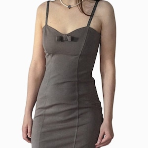 May include: A taupe-colored, fitted dress with a sweetheart neckline and thin, sparkly straps. A small bow detail accents the bust. The dress has a tailored silhouette, with vertical seams adding structure.