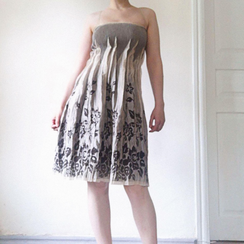 May include: A strapless dress with a beige and black floral pattern. The dress features a gathered bodice and a flowing skirt. The top portion of the dress is a darker shade of beige, while the skirt has a lighter beige background with black floral designs.