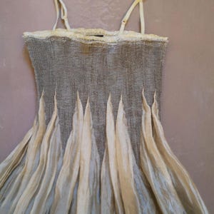 May include: A sleeveless dress with a textured gray bodice and a flowing, cream-colored skirt. The dress features delicate spaghetti straps and a lace trim at the neckline. The skirt has vertical, pointed accents.