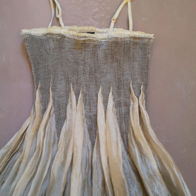 May include: A sleeveless dress with a textured gray bodice and a flowing, cream-colored skirt. The dress features delicate spaghetti straps and a lace trim at the neckline. The skirt has vertical, pointed accents.