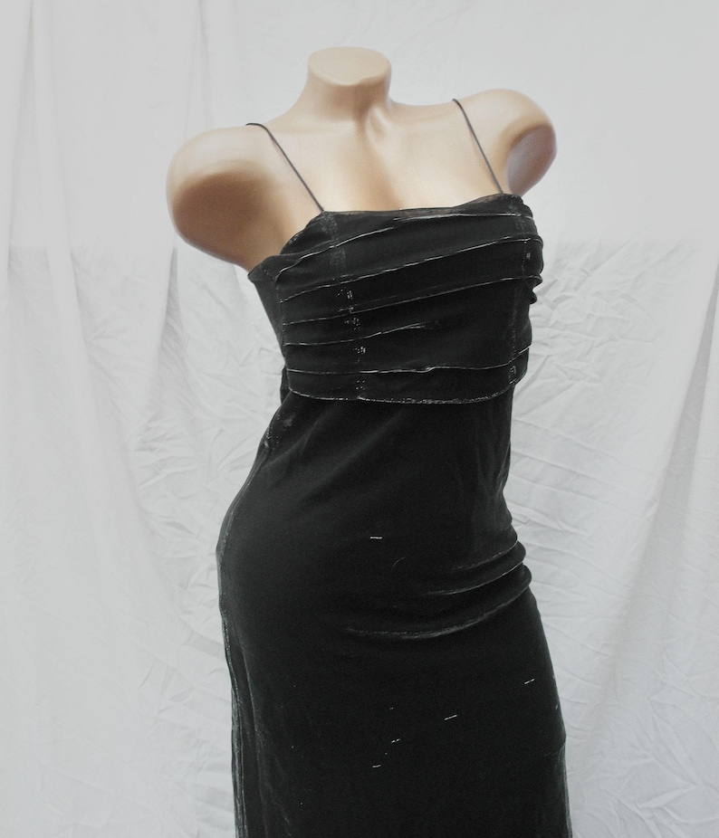 May include: A black sleeveless dress featuring thin spaghetti straps and a straight neckline. The bodice is detailed with horizontal fabric pleats across the chest, while the skirt falls in a straight, fitted silhouette made of a dark fabric.