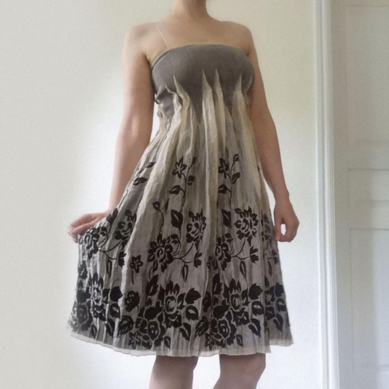 May include: A strapless dress featuring a taupe bodice and a flowing skirt. The skirt is a light beige color with a dark brown floral pattern. The dress is knee-length and appears to be made of a lightweight fabric.