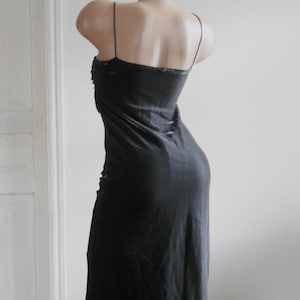 May include: A floor-length black slip dress featuring thin spaghetti straps and a straight neckline. The garment is displayed on a mannequin, showcasing a simple, unadorned silhouette that falls straight down from the bodice to the hemline.