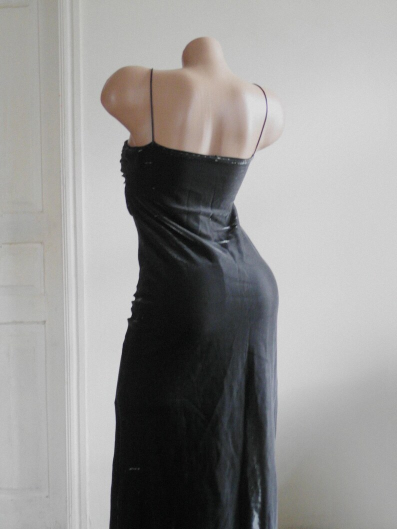 May include: A floor-length black slip dress featuring thin spaghetti straps and a straight neckline. The garment is displayed on a mannequin, showcasing a simple, unadorned silhouette that falls straight down from the bodice to the hemline.