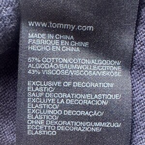 Puede incluir: Primer plano de una etiqueta de ropa azul marino oscuro con texto blanco. La etiqueta incluye la direcci&oacute;n del sitio web www.tommy.com y frases en varios idiomas, incluyendo "Made in China" y "Exclusive of Decoration".